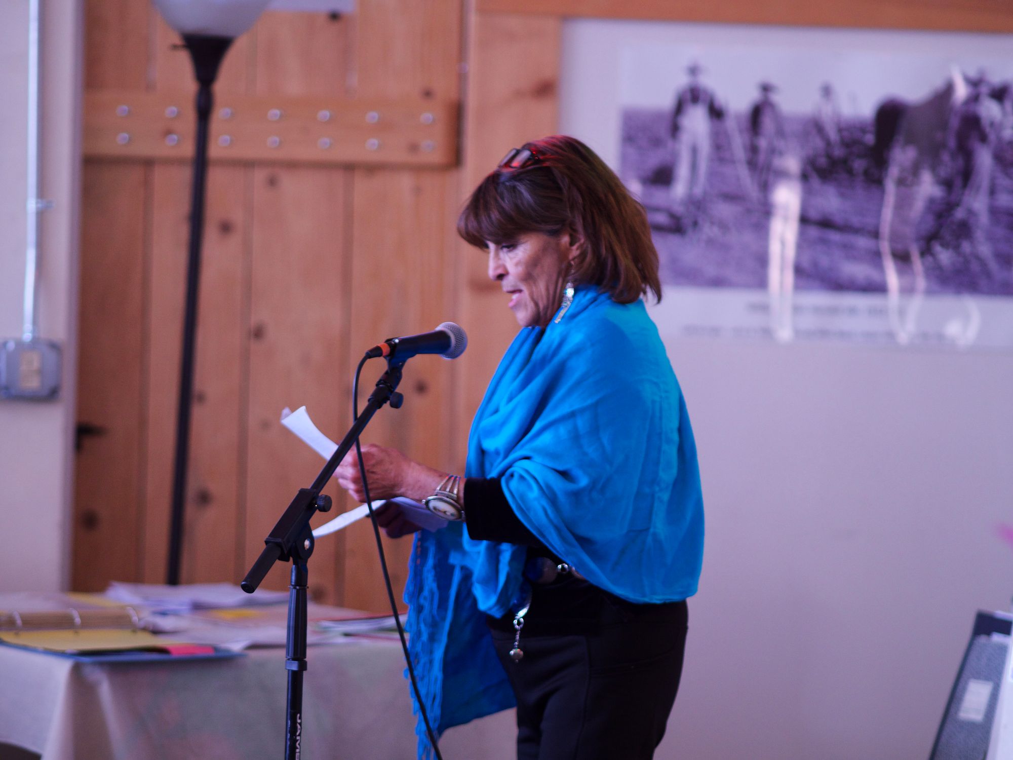 A woman speaks at a microphone while wearing a royal blue shawl and black clothing.
