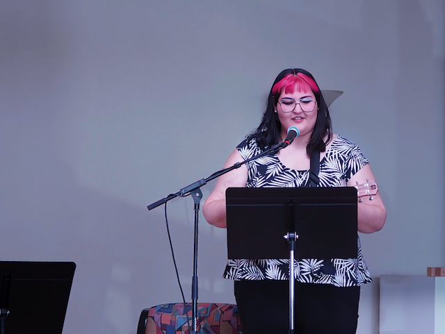 A woman performs behind a music stand with a ukulele