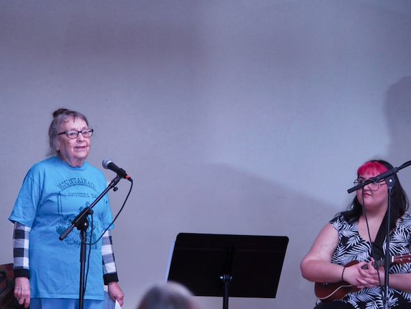 On the left is a woman speaking behind a microphone; on the right is a woman seated with a ukulele.